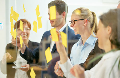 Menschen lesen gelbe Post-it-Zettel an einer Glaswand